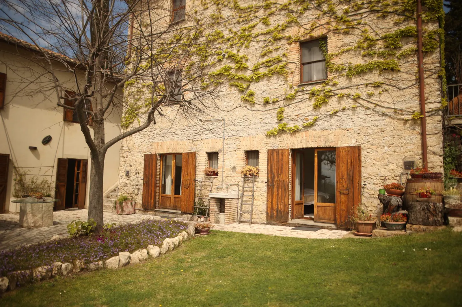 Steinhaus mit Weinranken, Holzläden und Garten mit Rasen und Blumenbeet