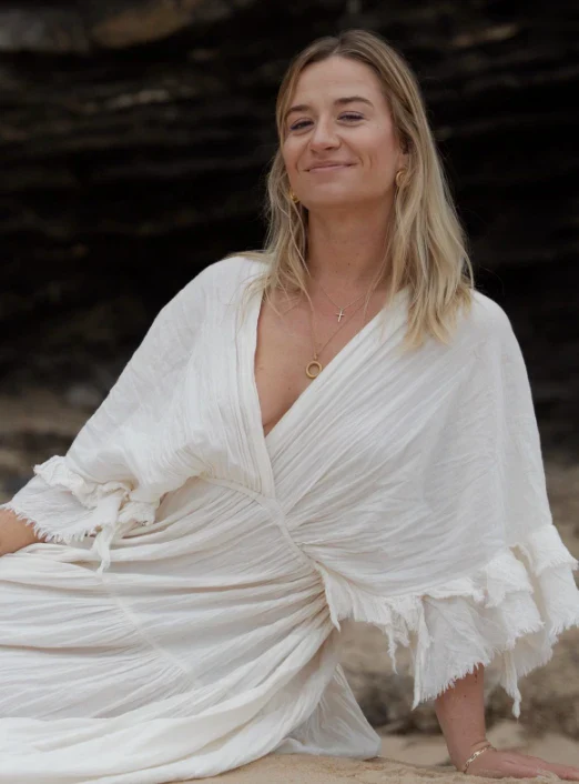 Rina in einem weissen Leinenkleid am Strand, lächelnd
