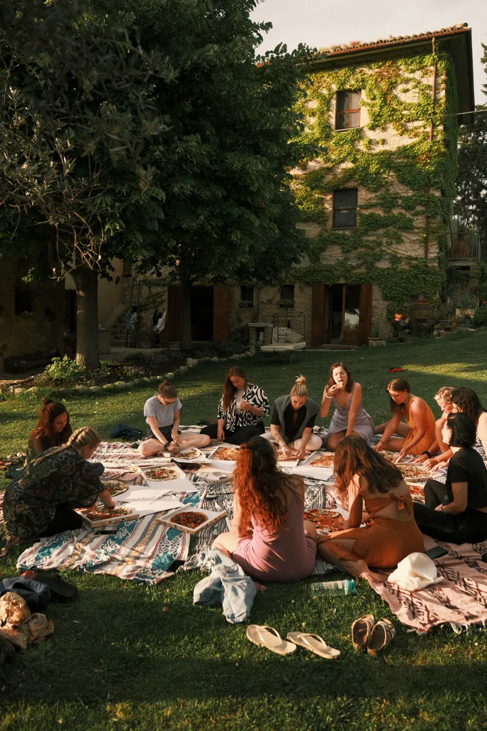 Frauen beim gemeinsamen Picknick auf Decken im Garten vor dem Steinhaus